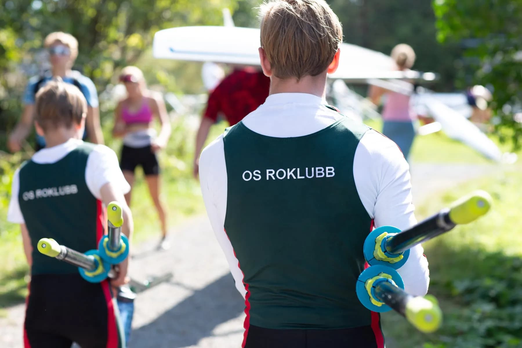 Unge roere i Os Roklubb-drakter bærer årer og båt ned mot vannet